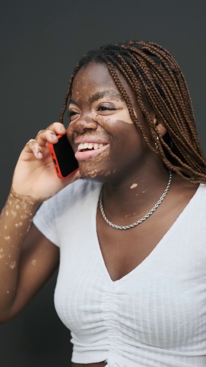 一个患白癜风的非裔美国妇女在打电话时微笑的特写镜头。视频下载