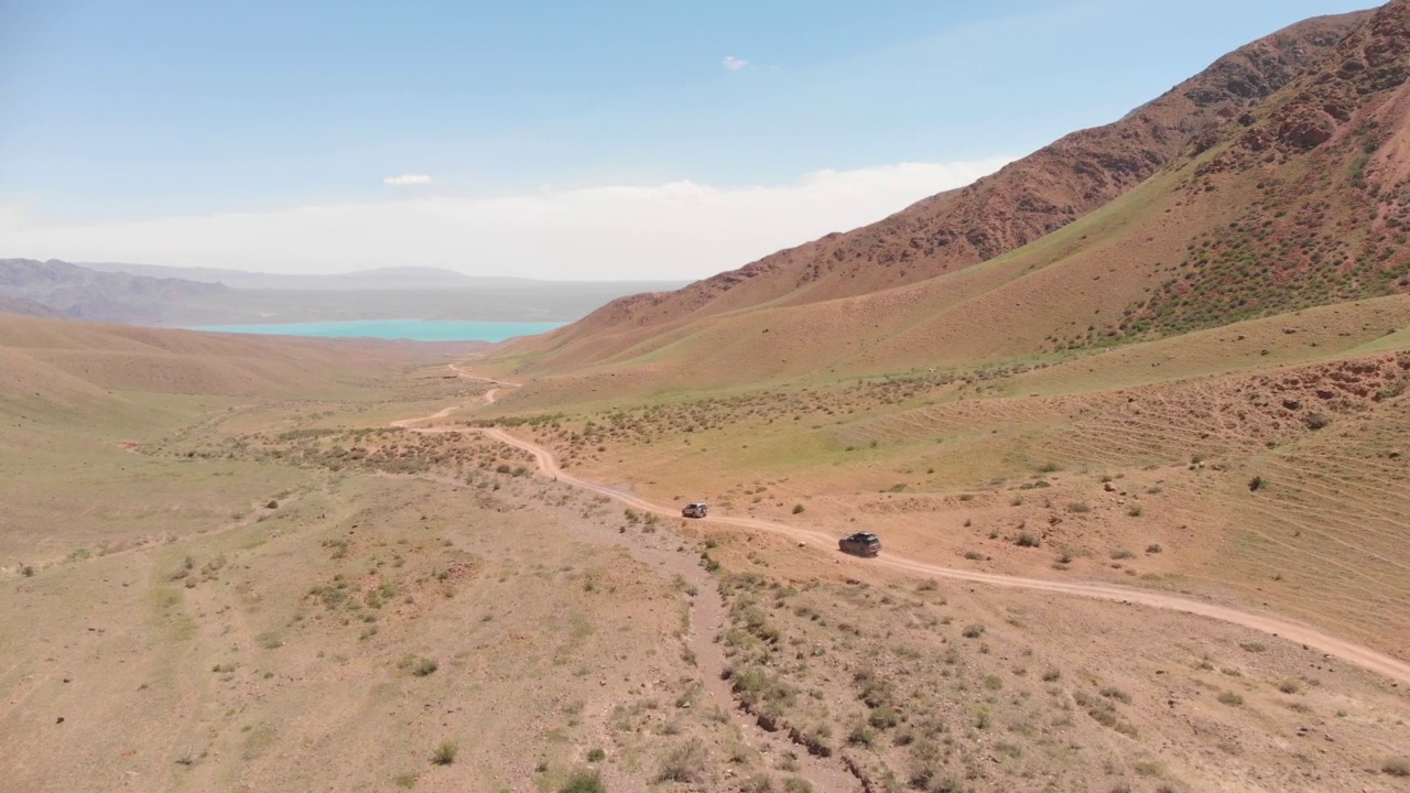 两辆suv在山间行驶，沿着一条土路驶向一个美丽的山间湖。视频素材