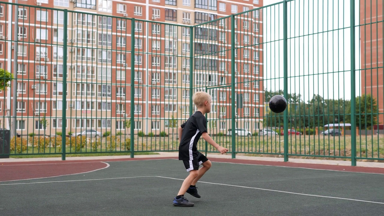一个男孩在院子里的橡胶操场上用足球训练。视频下载