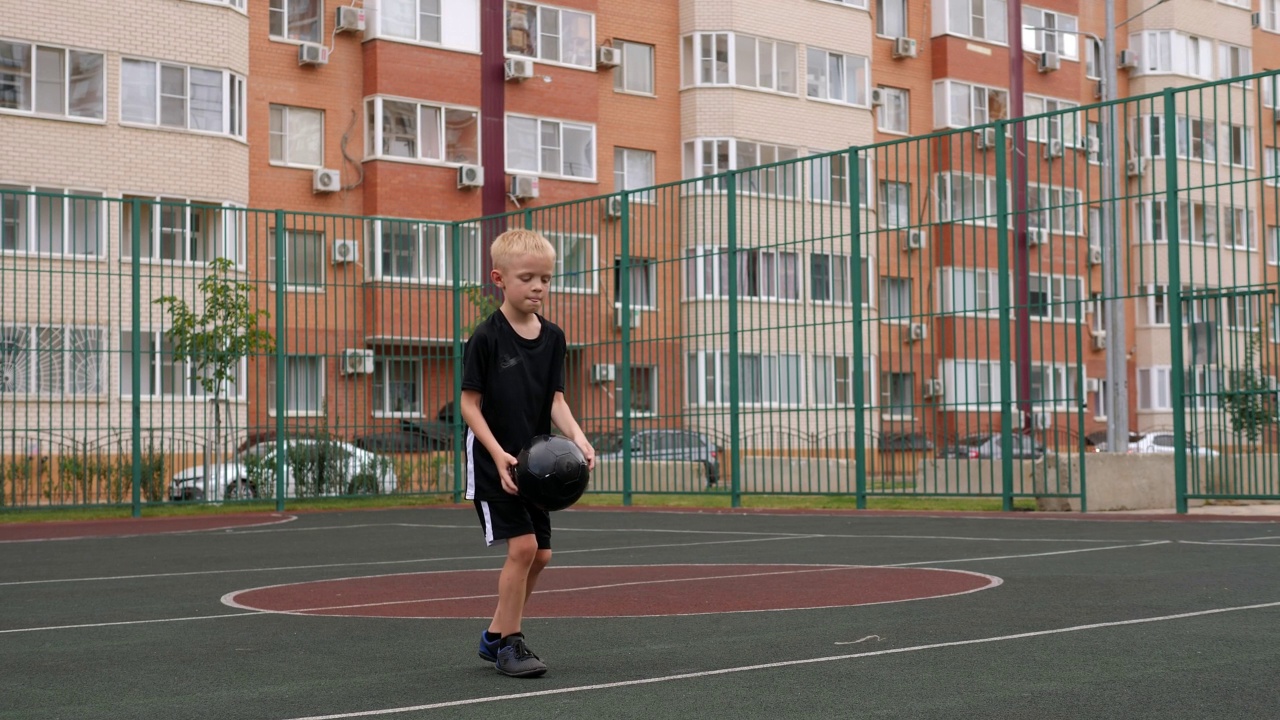 这个男孩正在城里院子里的操场上踢足球。视频下载