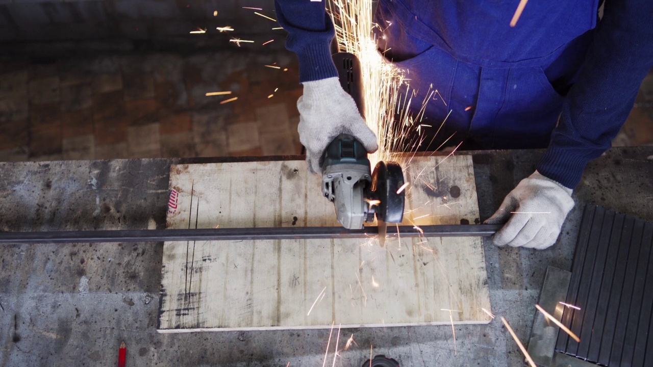 追踪无法辨认的金属工人戴着防护手套，用角磨机均匀切割金属板的右上方视图。火花从切割轮上飞离视频下载