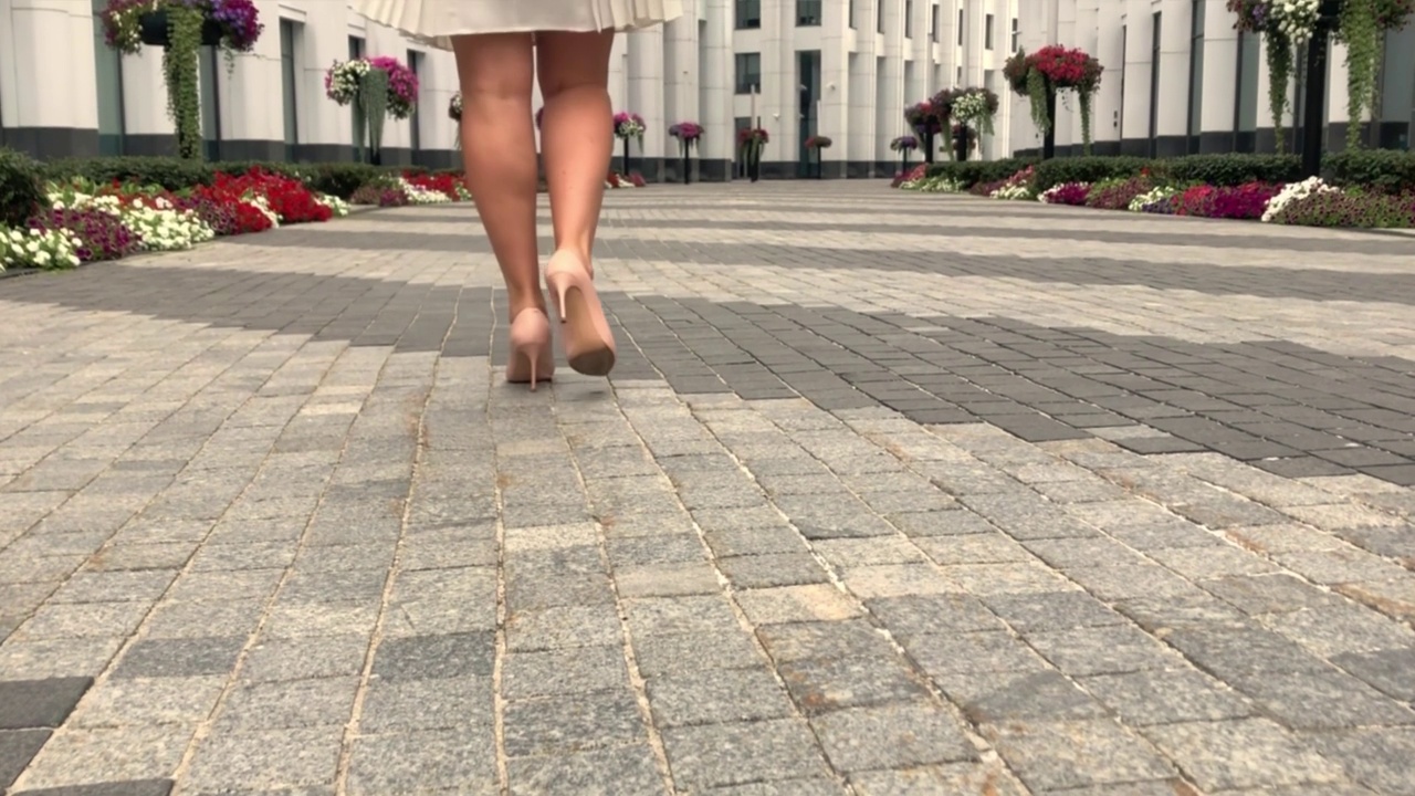 穿着米色高跟鞋的女人们的腿走在高楼大厦旁的马路上。商业风格服装视频素材