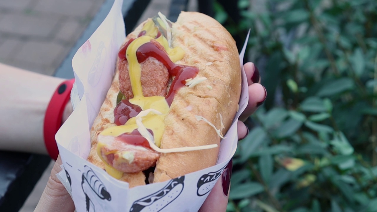 手里拿着热狗，香肠和番茄酱夹在白面包里。视频下载