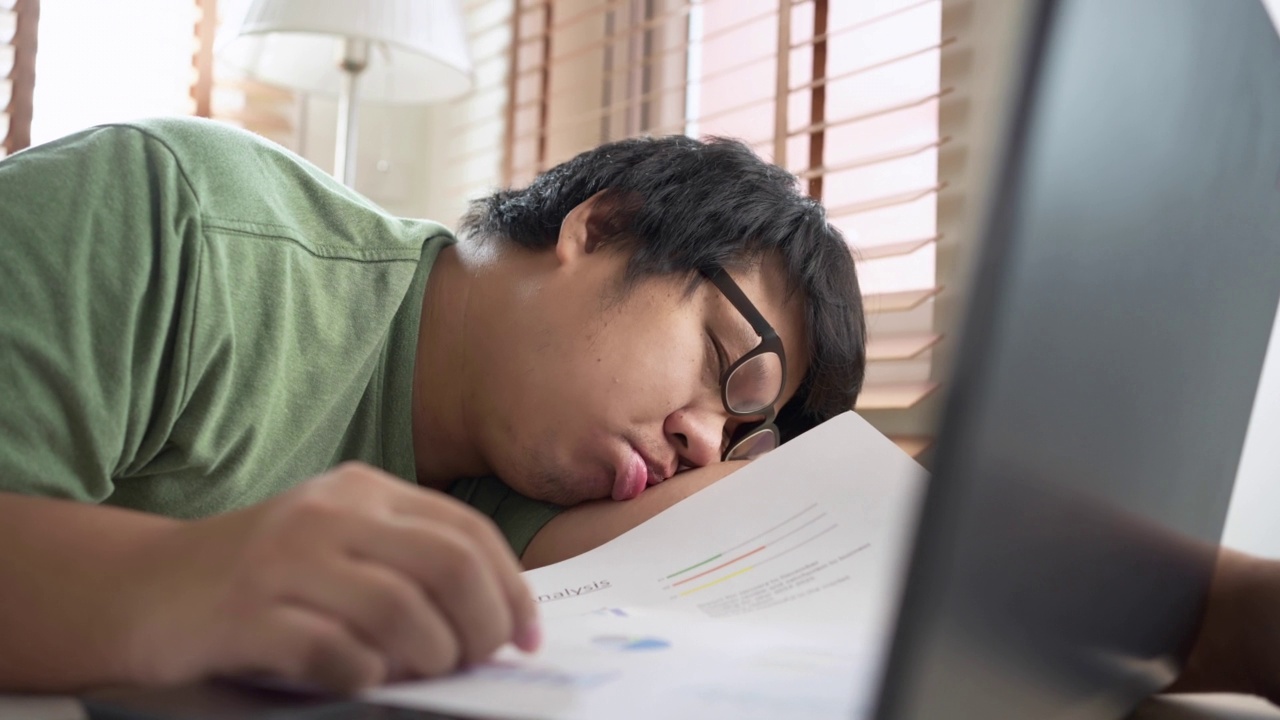 我试过一个亚洲人在家里用笔记本电脑工作时睡在桌子上。一份自由职业的工作视频素材