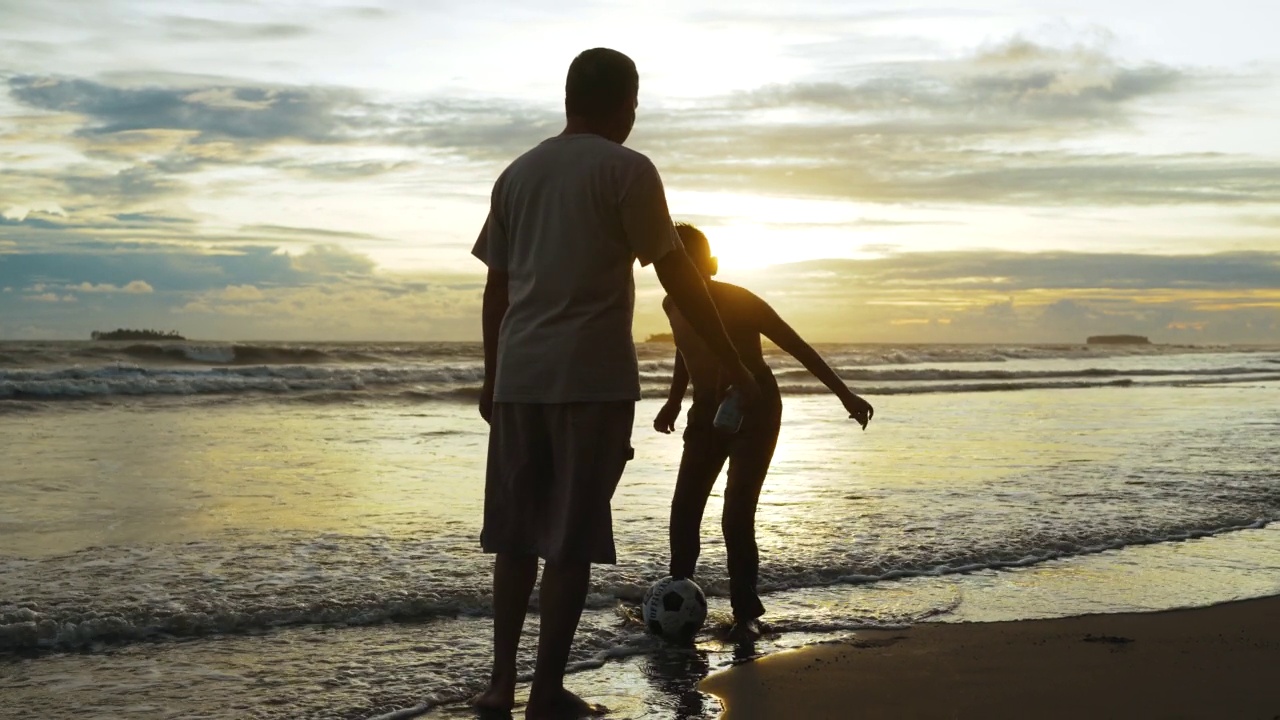 夕阳西下，幸福的父亲和儿子在海滩上踢足球。幸福的一家人在海滩上享受暑假。假日旅行的概念。假期视频素材