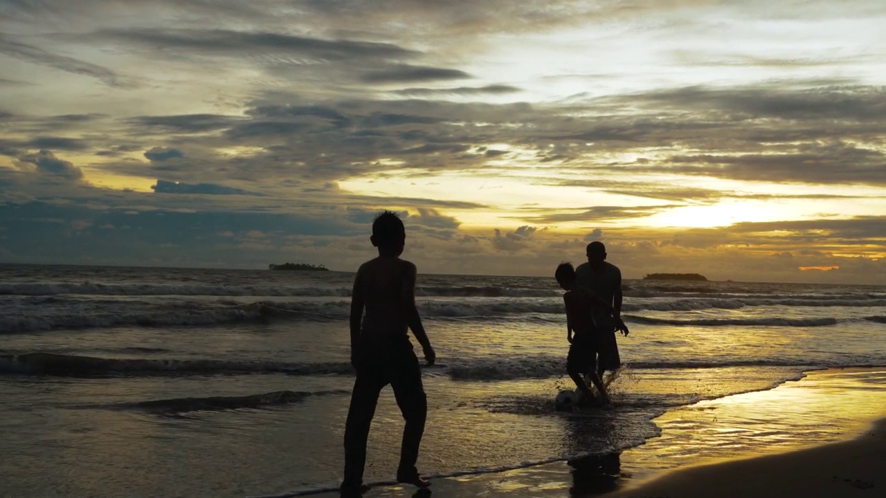夕阳西下，幸福的父亲和儿子在海滩上踢足球。幸福的一家人在海滩上享受暑假。假日旅行的概念。假期视频购买