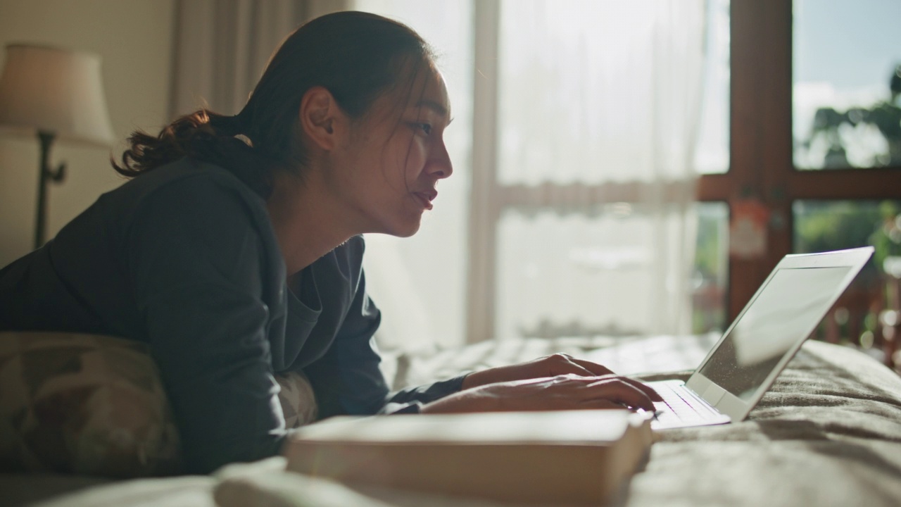 亚洲妇女在家里的床上使用笔记本电脑视频素材