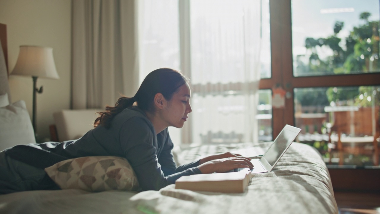 亚洲妇女在家里的床上使用笔记本电脑视频素材