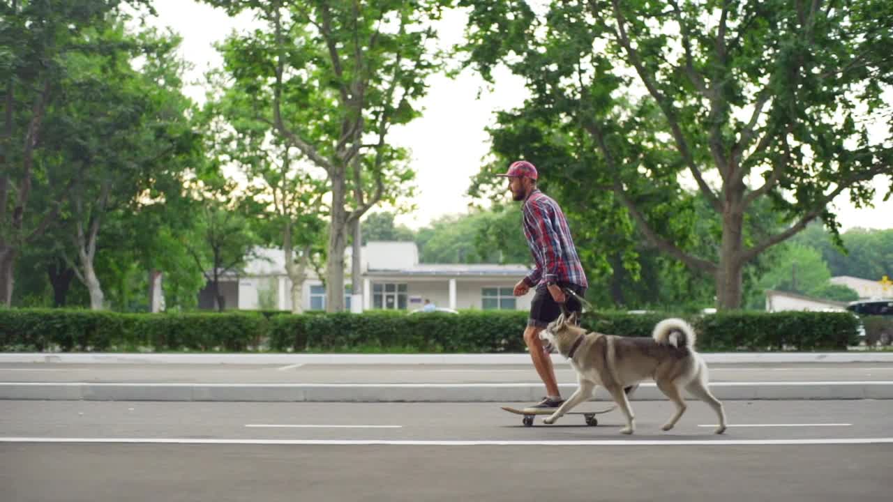 年轻的潮男孩骑滑板与哈士奇狗牵引阳光慢动作快速视频素材