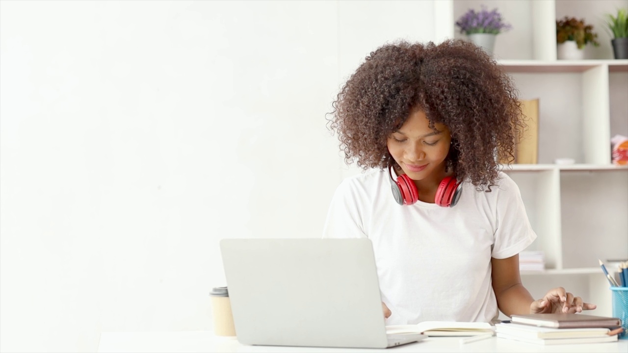 美国少女坐在白色的办公室里拿着笔记本电脑，她是一名学生在家里用笔记本电脑在线学习，大学生在线学习，在线网络教育的概念。视频素材