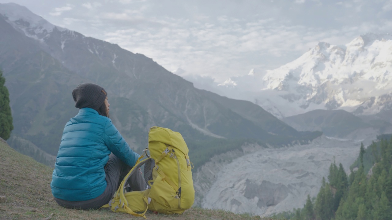 后视图，快乐的自由旅行者年轻的妇女穿着蓝色的冬季夹克坐在山顶享受旅游假期在冬天的早晨。种族多元化的旅行者概念。与α香奈儿。视频素材