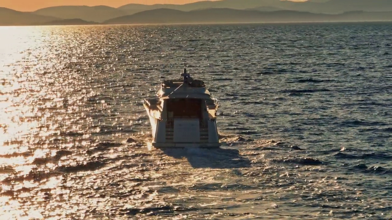 当太阳落在岛屿后面时，空中游艇在海上巡航视频素材