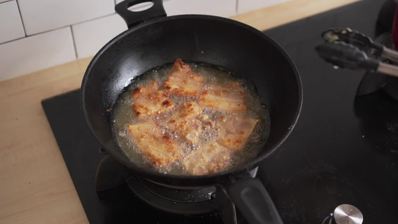 在自家厨房用油锅煎香脆的五花肉。不健康的亚洲食物高胆固醇的肉类准备晚餐视频素材