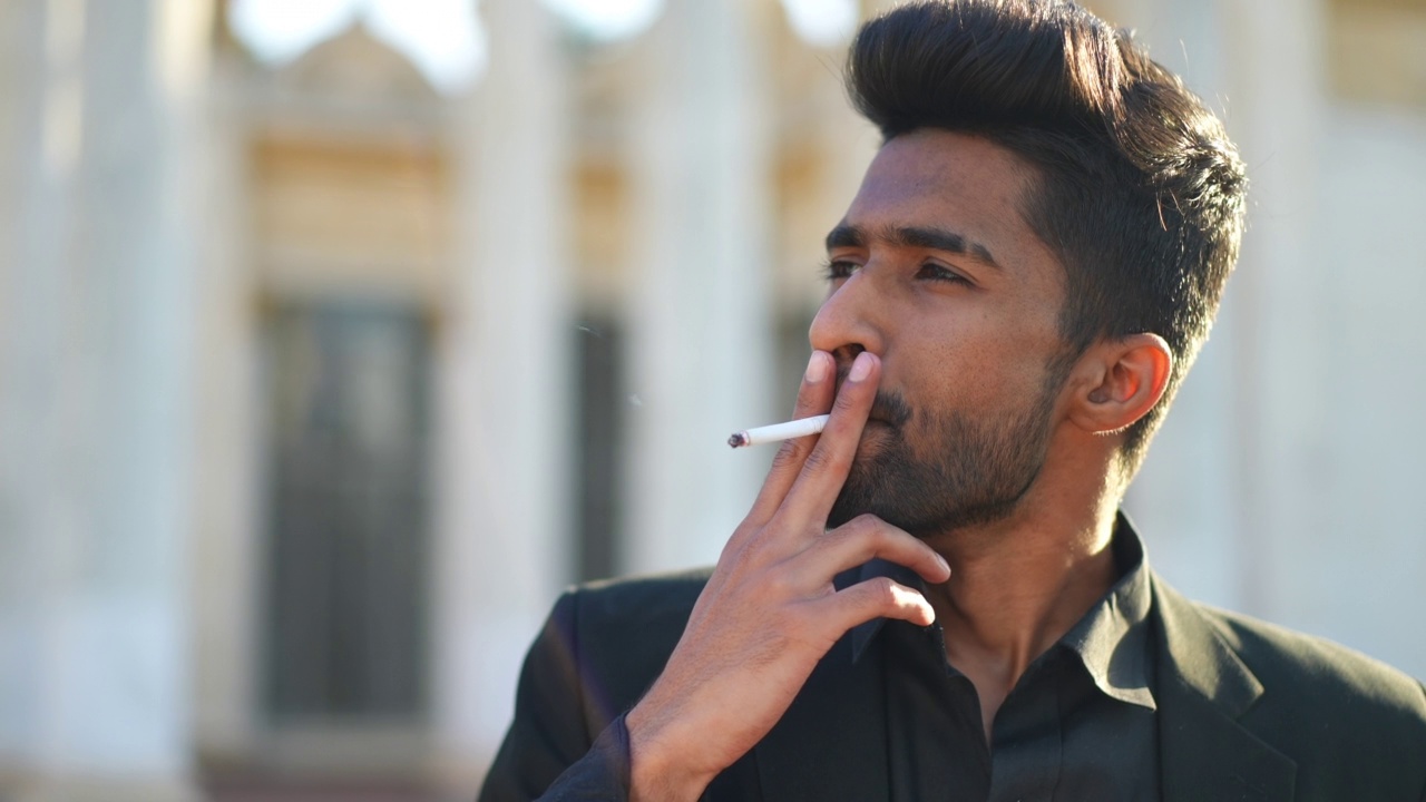 特写画像微笑的中东青年吸烟说话站在城市的城市街道。阳光下快乐自信的帅哥。有害的习惯和生活方式观念。视频下载