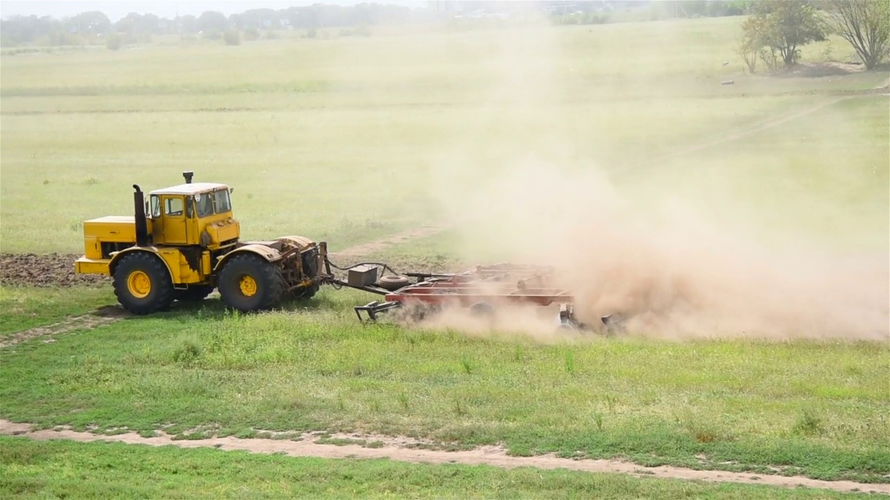 黄色的拖拉机培育绿色的田野。视频下载
