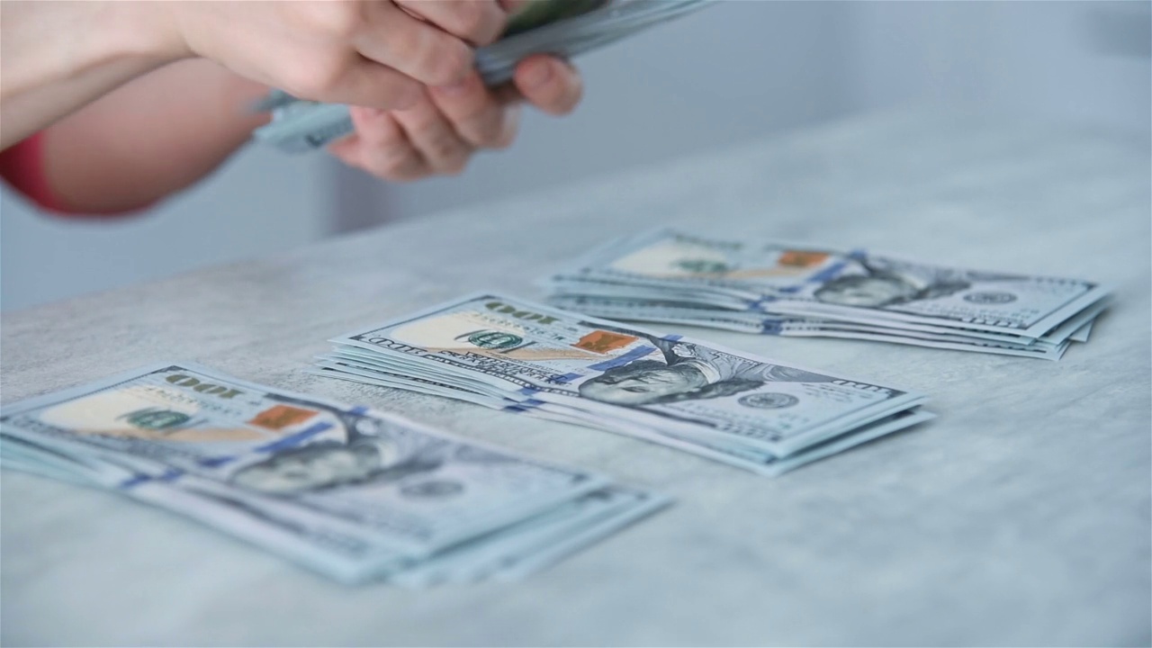 女商人用手在桌子上数美元钞票。视频下载