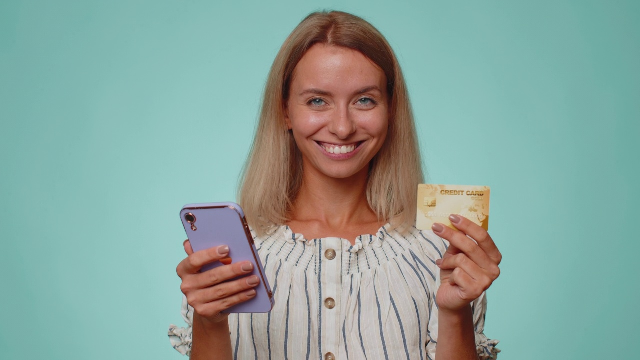 年轻女子在网上购物时使用信用卡和智能手机转账视频素材