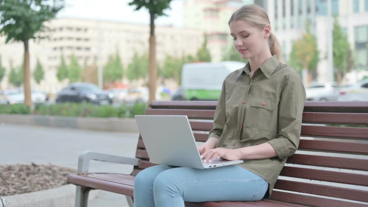 拿着笔记本电脑的妇女坐在户外长凳上时竖起大拇指视频素材