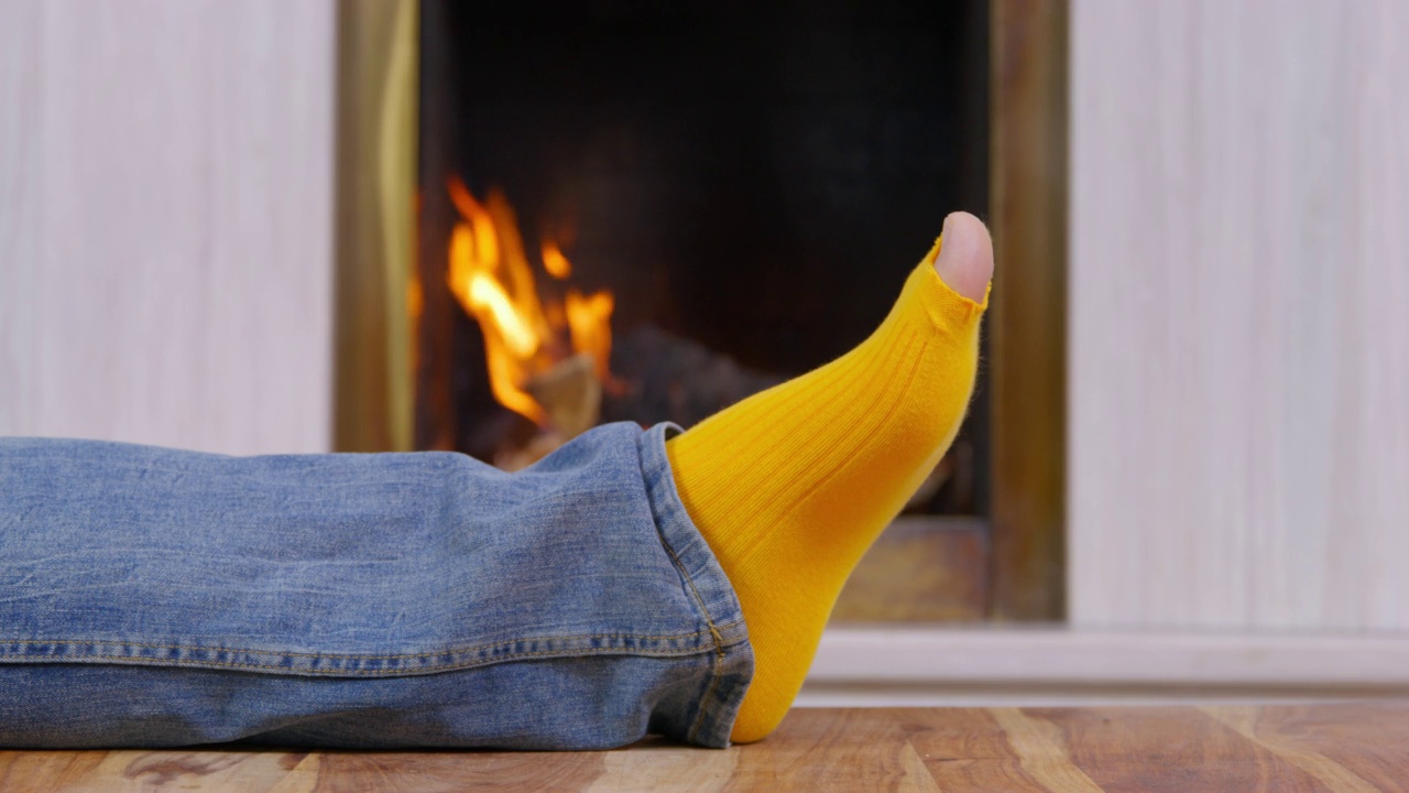 人的腿在燃烧的壁炉前的地板上，袜子有洞。视频下载