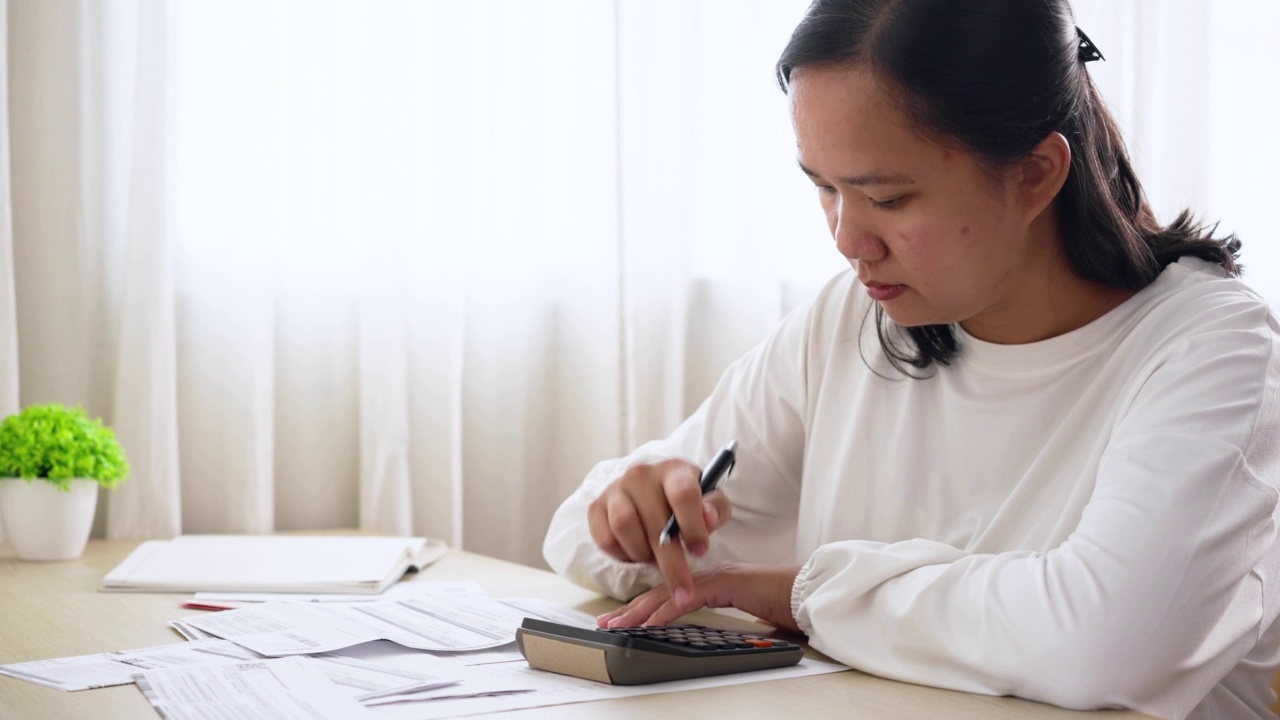 亚洲妇女使用计算器管理家庭财务和账单报表。家庭财务规划视频素材