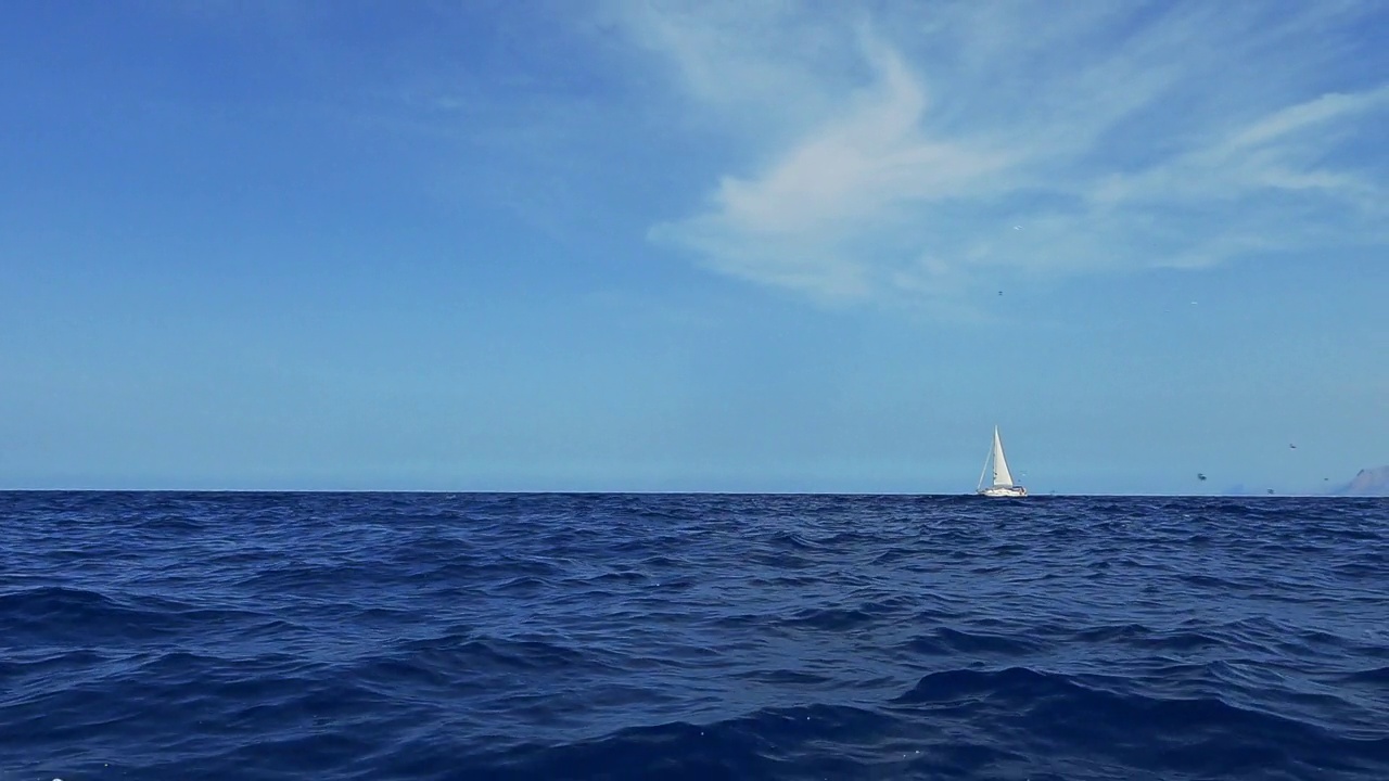 从另一艘巡航船上看到的在海水中航行的帆船的低角度水面视图。慢动作视频素材
