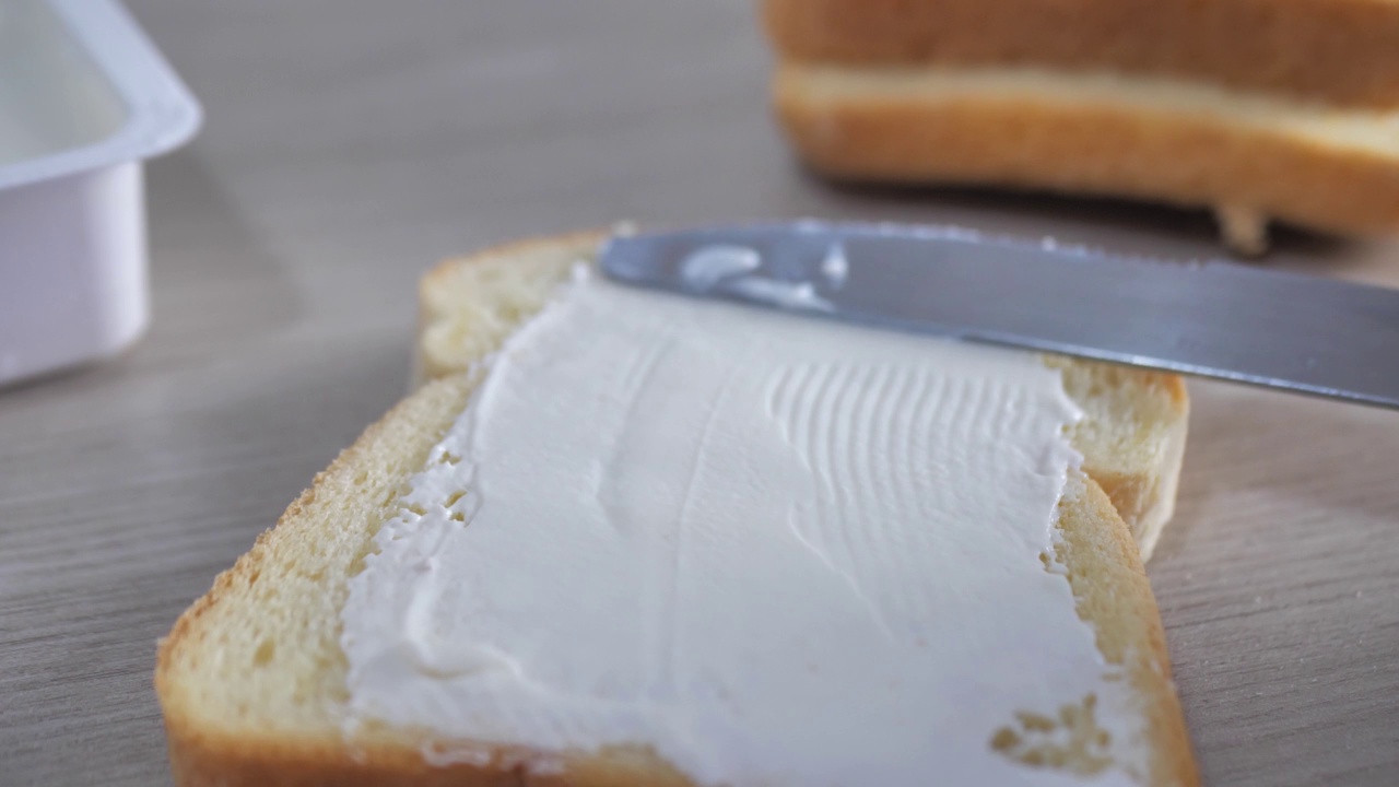 用厨房桌上的黄油刀把奶酪糊涂在烤好的面包上视频下载