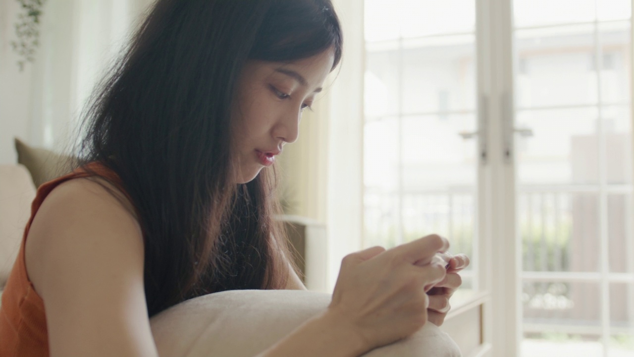 亚洲妇女拿着智能手机在客厅玩游戏。视频素材