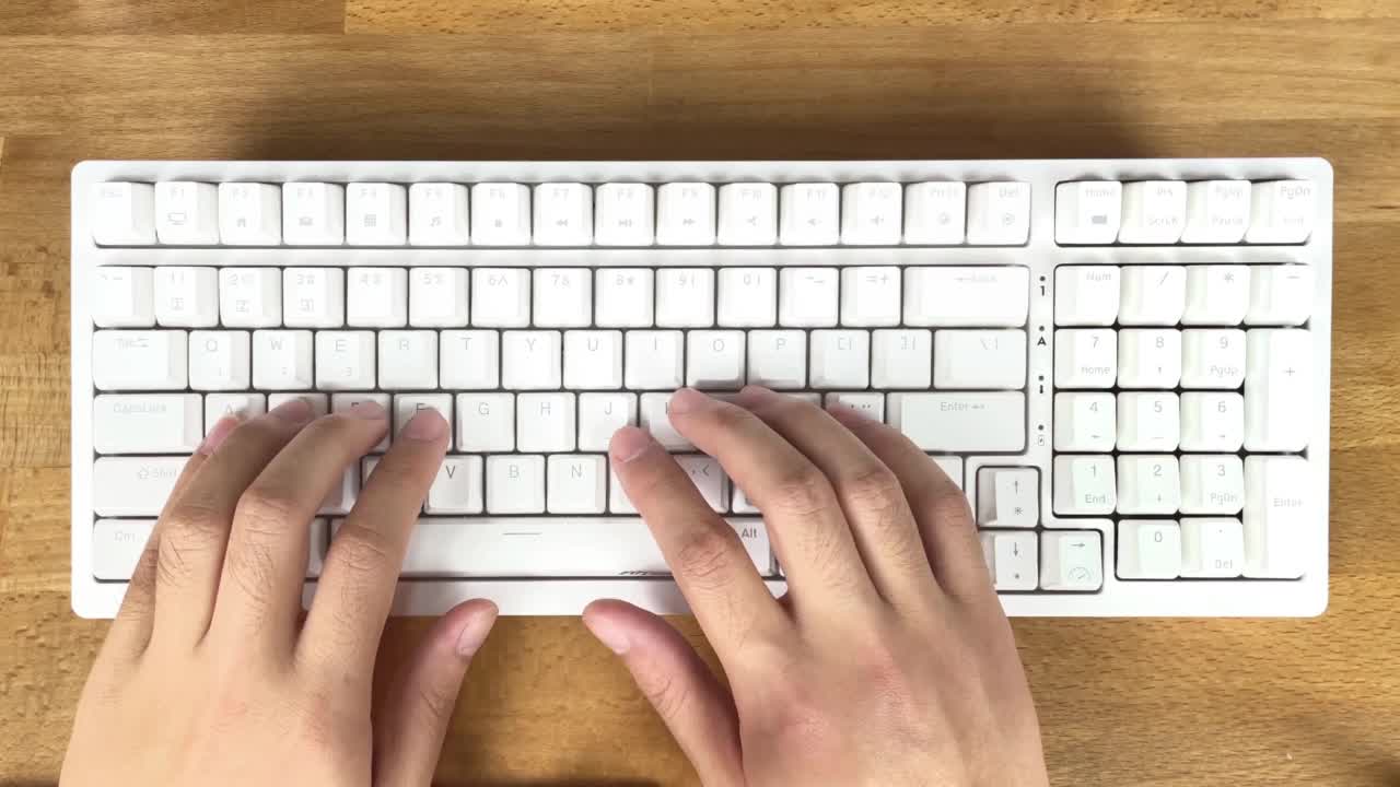 男人的手在白色的键盘上打字，在一张木桌上工作视频素材