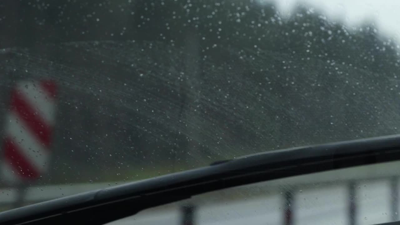雨点在汽车前窗上的特写和雨刷的运动。车辆驶来的模糊轮廓视频素材