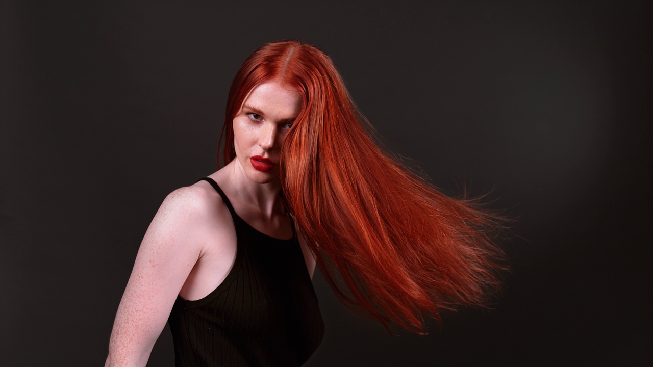 迷人的红发女子在镜头前甩着她又长又健康的头发。演播室拍摄，超慢动作视频下载