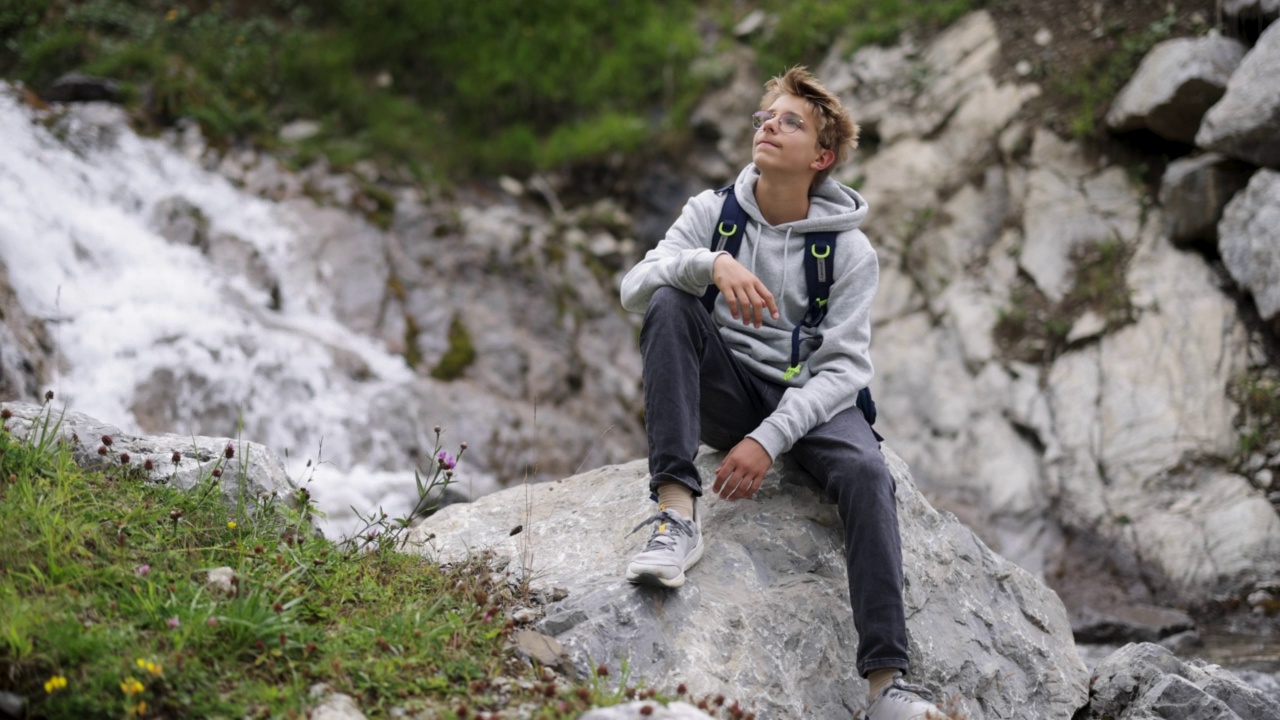 少年徒步旅行者坐在奥地利山脉的瀑布附近-阿尔卑斯山，Vorarlberg，奥地利。视频下载