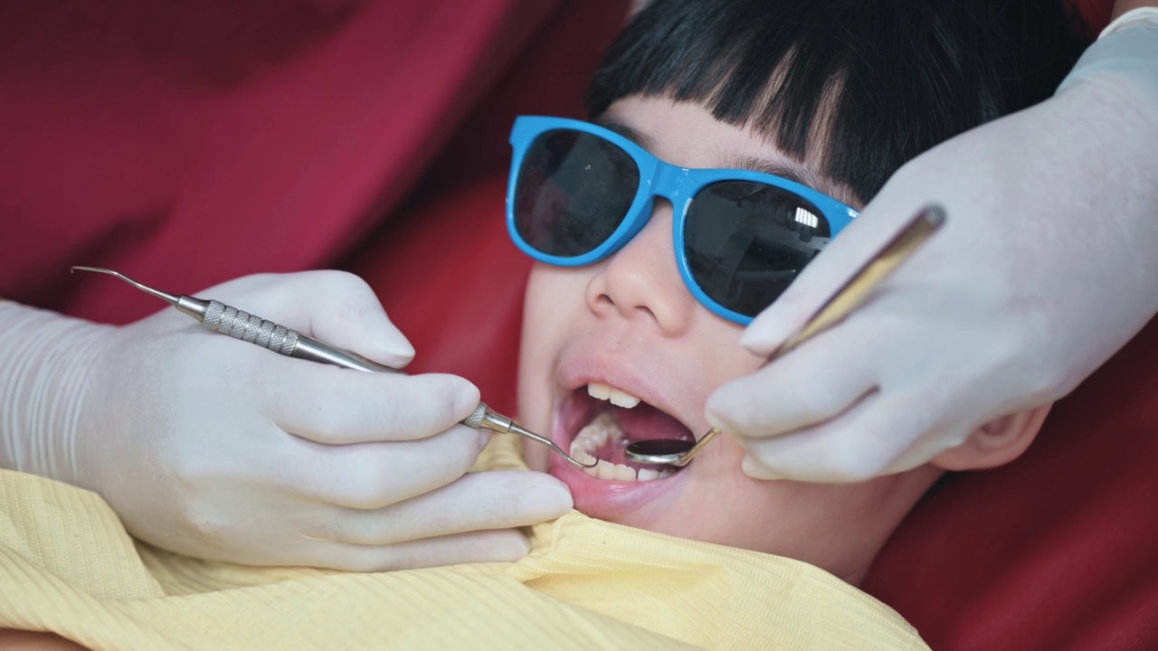 近距离的亚洲华人牙医在牙医办公室用斜角镜检查小男孩的牙齿视频素材