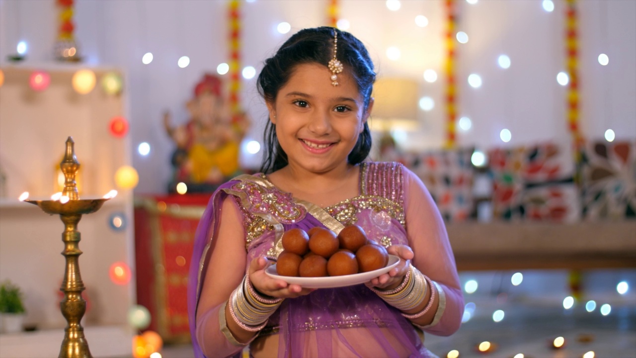 一个甜美的印度女孩在排灯节庆祝期间提供古拉布- Jamuns -传统的印度糖果，印度排灯节，排灯节装饰视频素材