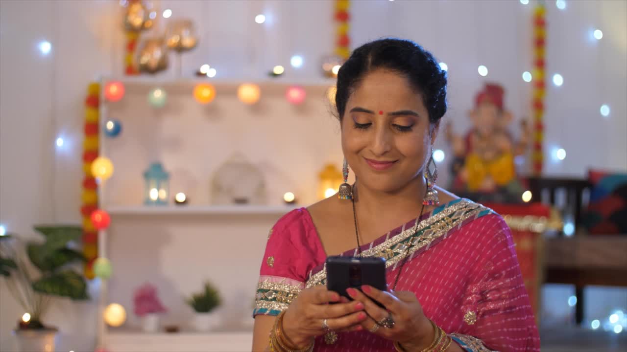 一名印度妇女站在五彩缤纷的背景下，用鲜花和彩灯装饰着手机，查看她的信息视频素材