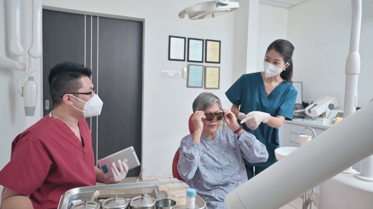 亚裔华人牙医在女护士的帮助下调整手术灯，准备为老年女性患者进行牙科手术视频素材