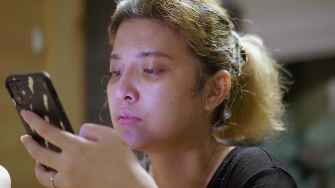亚洲妇女在家里的客厅用智能手机打字。视频素材