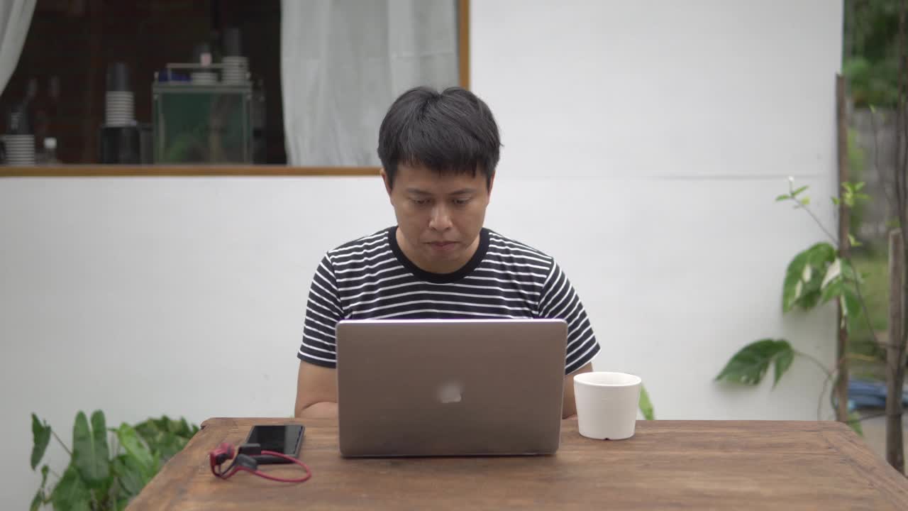 亚洲男子坐在外面用笔记本电脑工作。视频下载