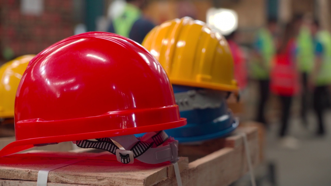 工人手持头盔的特写，许多安全头盔放在仓库商店为员工准备的纸箱上，红色、白色和黄色的硬头盔为工程师检查工业视频下载