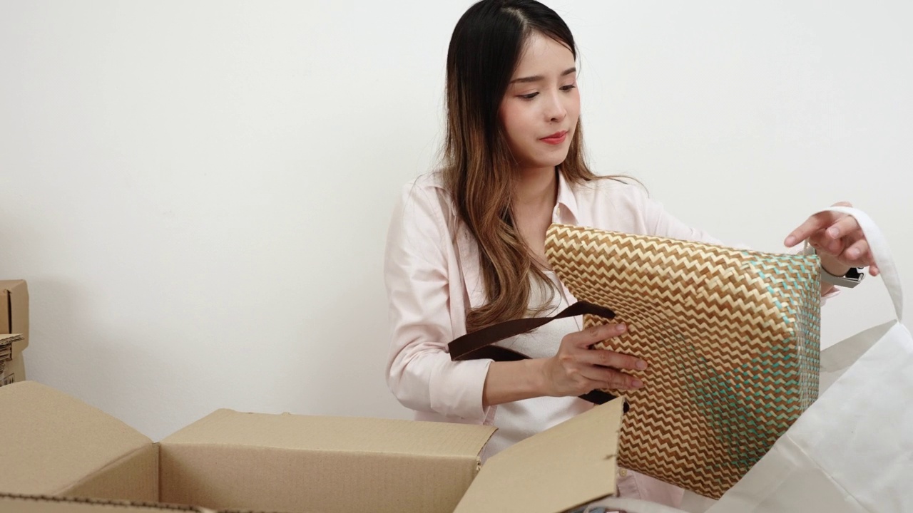 在网上销售的妇女把用草制成的手提包放在盒子里，准备把包裹寄给顾客。视频下载