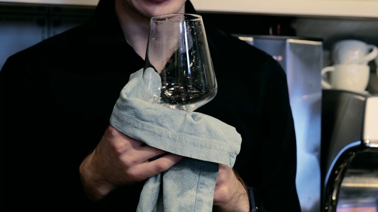 一位职业酒保的手正在用一块灰色的布擦拭玻璃杯。视频下载