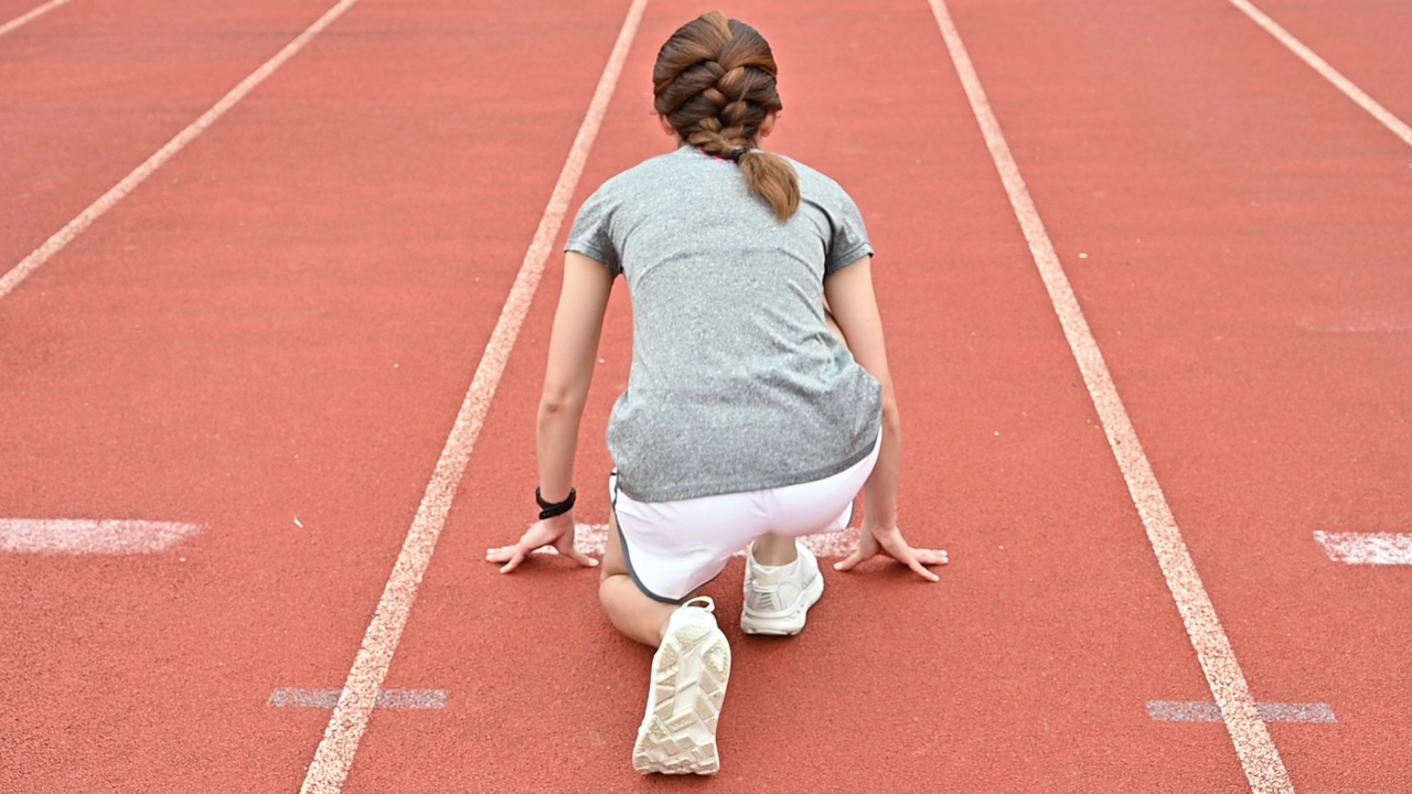 慢动作镜头的女运动员在开始位置准备冲刺在跑道在体育场。视频素材