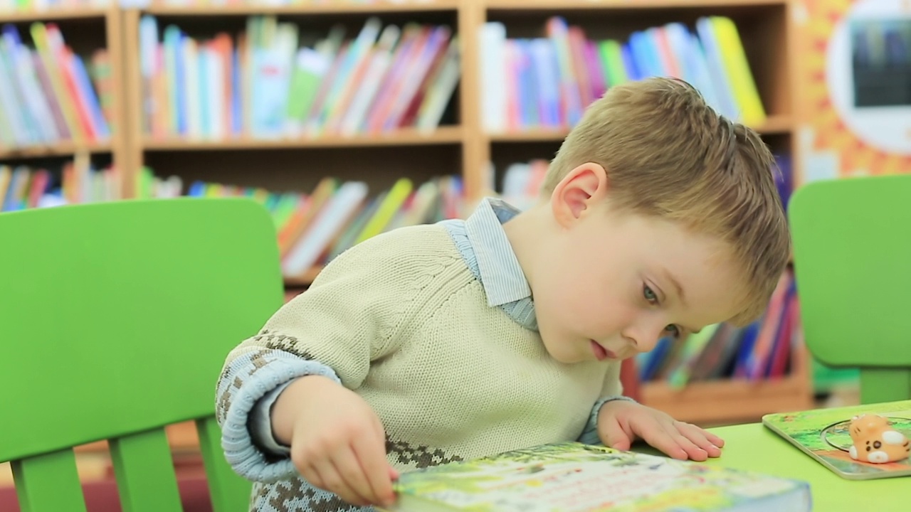 一个小男孩在图书馆里研究一本儿童图画书视频素材