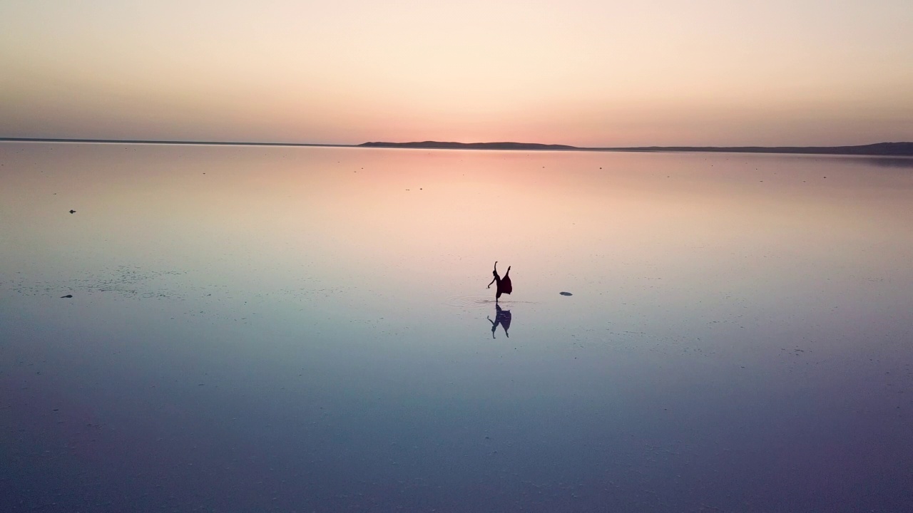 无人机拍摄的芭蕾舞者在日落时在图兹湖跳舞，以及她在水中的倒影视频素材