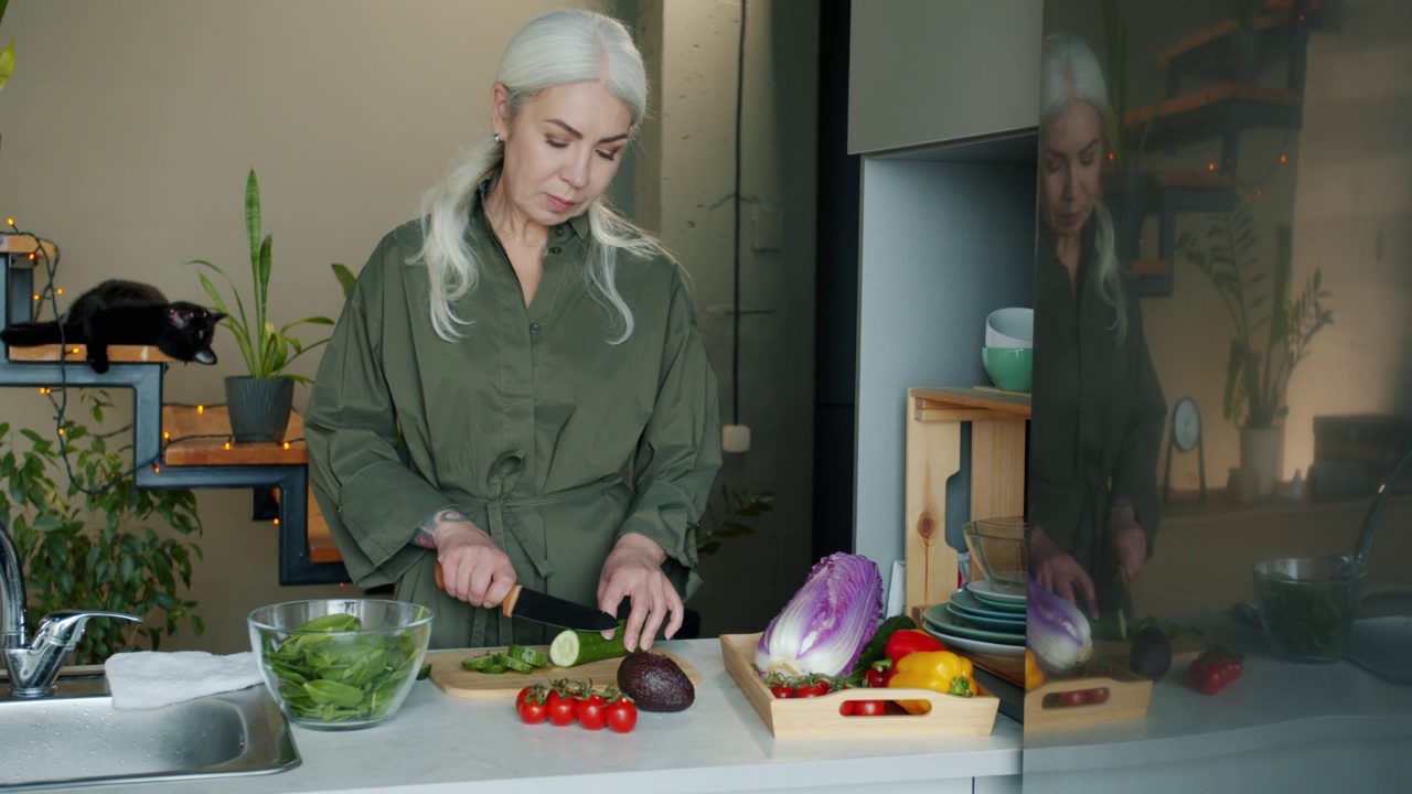 在厨房里用刀切黄瓜的成熟女士的画像视频素材