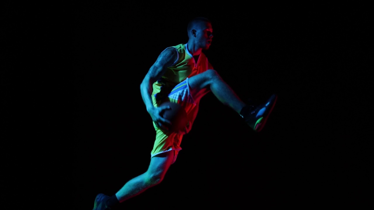 身穿黄色运动服的活跃篮球运动员在暗色背景的演播室拿着篮球跳跃。运动，动作，动作，技能概念视频素材