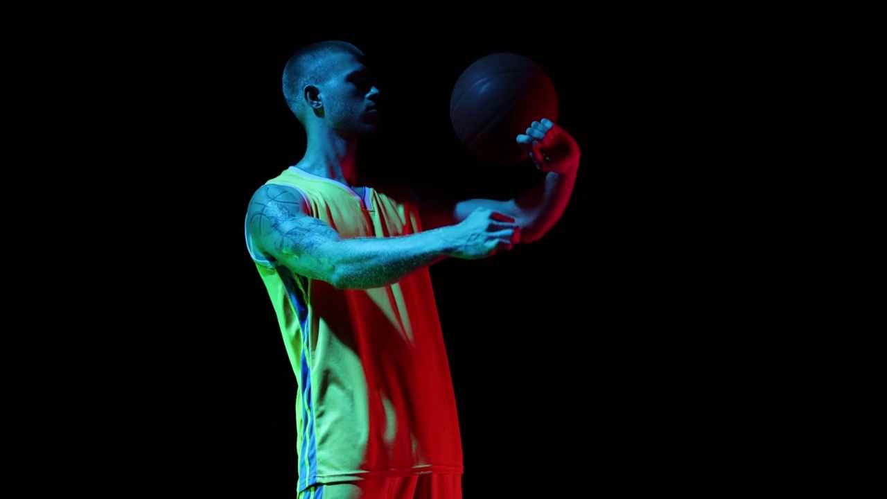 年轻人，篮球运动员旋转篮球在他的手在工作室在霓虹灯的黑暗背景。运动，动作，动作，技能概念视频素材