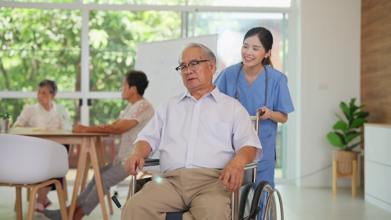 年轻的亚洲护理医生在养老院的客厅里推着坐在轮椅上的老人。精神保健和健康。护士带着微笑照顾老人和理疗视频下载