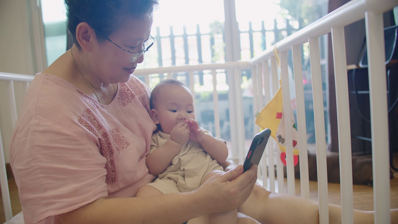 快乐的亚洲一代家庭高级奶奶和孙女婴儿学步享受科技使用智能手机自拍视频电话聊天聊天的父母在家里，在线交流的家庭概念视频素材