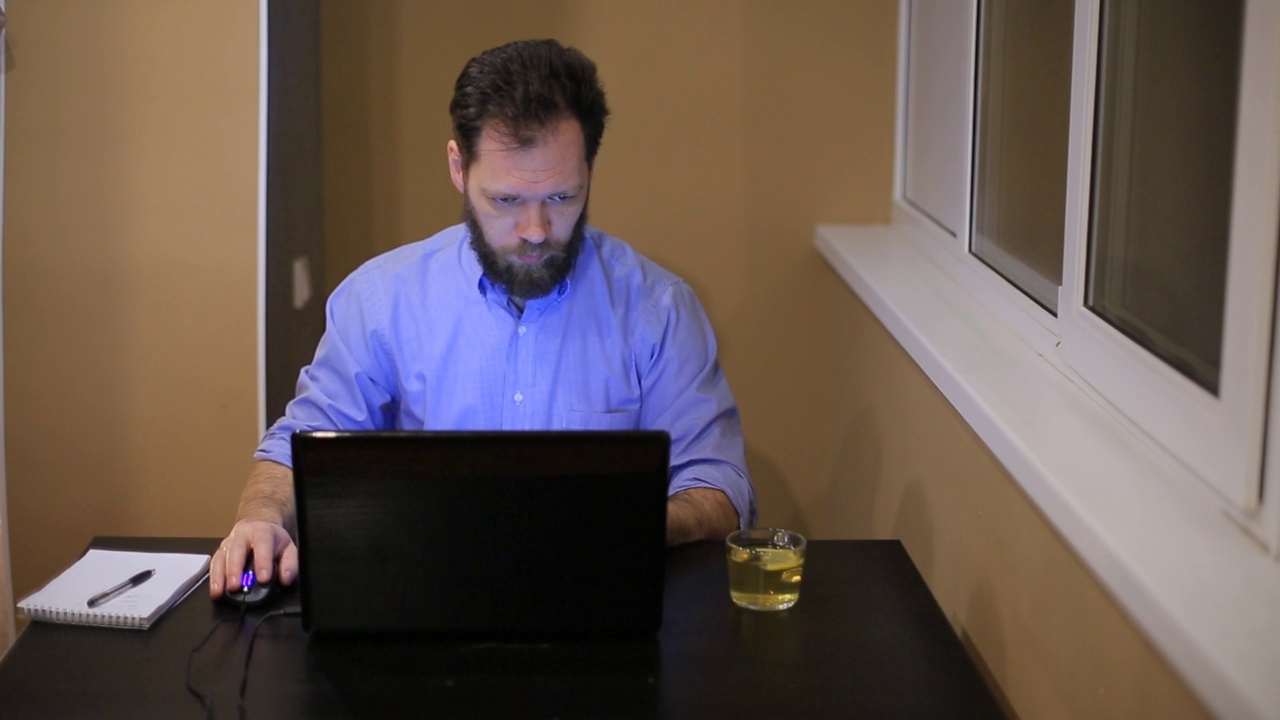 穿着蓝色衬衫和蓝色领带的严肃男人晚上在办公室用笔记本电脑工作视频下载