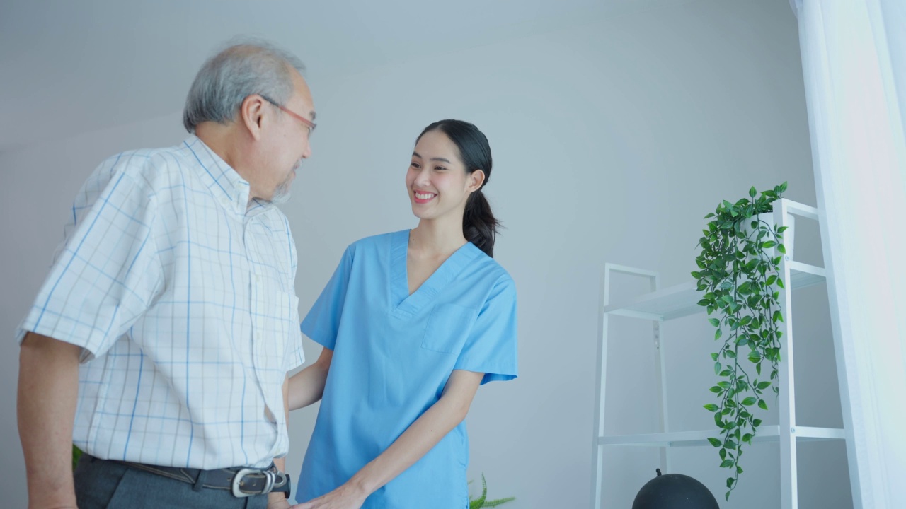 亚洲老年男性患者与护工进行物理治疗。有魅力的专业护工女性帮助和支持年长的成熟男性在养老院用助步器练习慢慢走路。视频下载